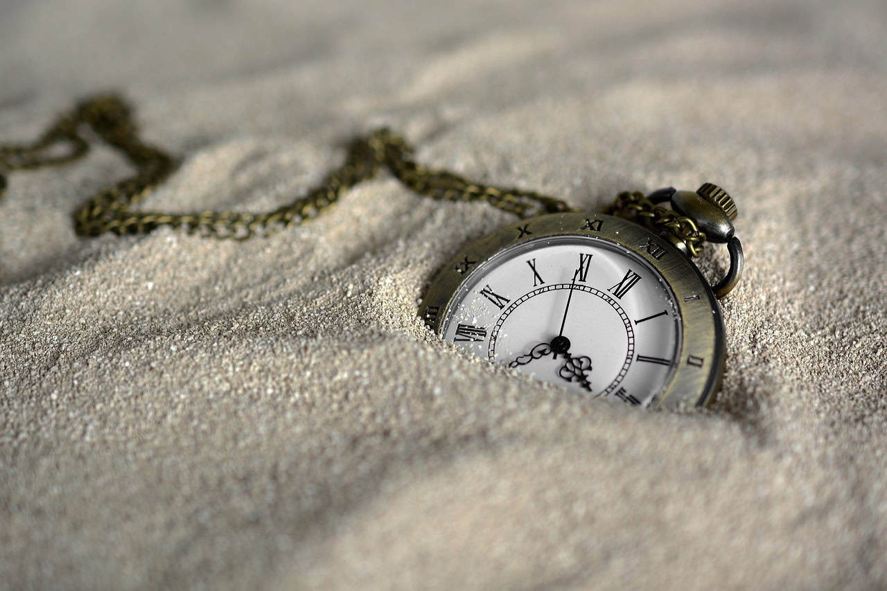 A pocket watch partially buried in sand, symbolizing exhaustion.